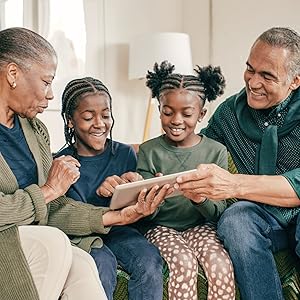 Grandparents sitting on a couch with two grandchildren, all interacting with a digital tablet